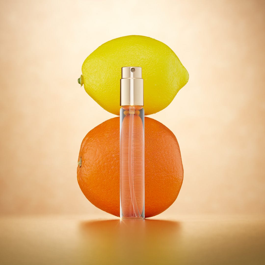 Veronique Gabai's booster Eau du Jour in a 10ml travel spray displayed in front of an orange and lemon, indicating its citrus notes.