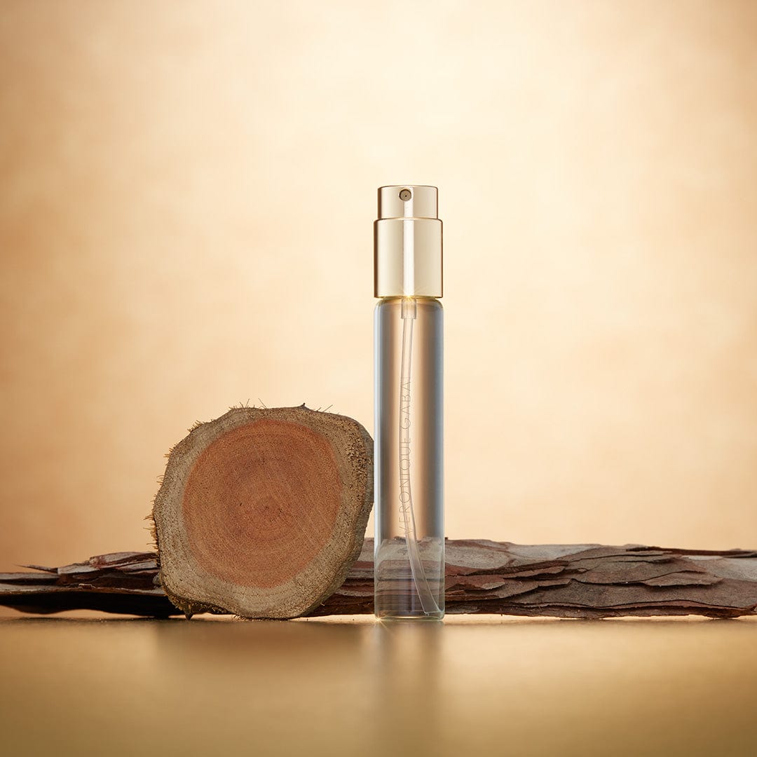 Veronique Gabai's booster Eau de la Nuit in a 10ml spray, displayed alongside wood, its key ingredient, in front of a gold background